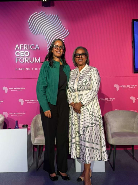Two women standing together on stage against a pink backdrop at an event